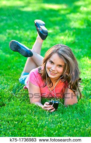 Young girl lying on grass listening to music View Large Photo Image Stock Image - Young girl lying on grass listening to music. Fotosearch