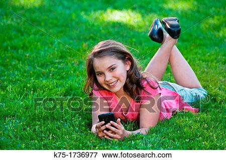 Stock Photo - young girl lying on lawn listening to music. Fotosearch