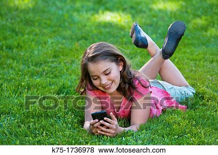 Young girl lying on lawn listening to music View Large Photo Image Stock Photo - Young girl lying on lawn listening to music. Fotosearch