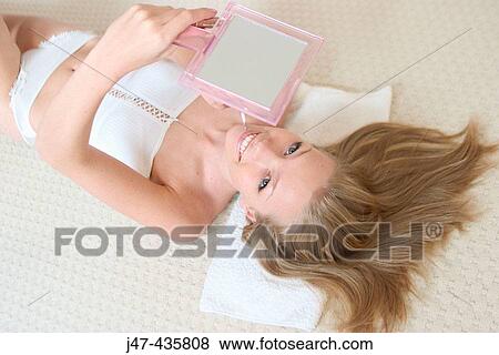 Stock Photo - Young girl lying on the floor, on her back, with a mirror, smiling into camera. Fotosearch
