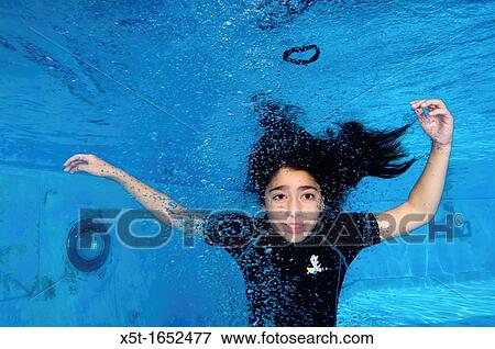 Stock Photo - Young girl of 9 holds her breath while floating underwater in a swimming pool. Fotosearch