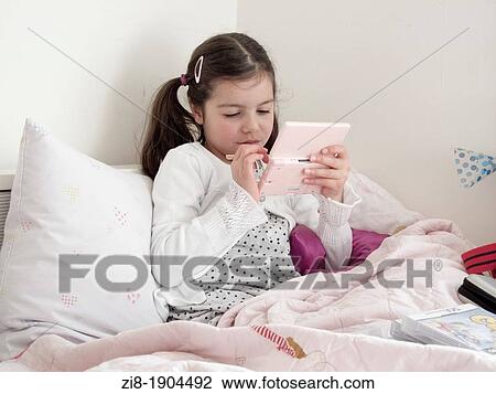 Stock Image - Young girl plays computer game in bed. Fotosearch