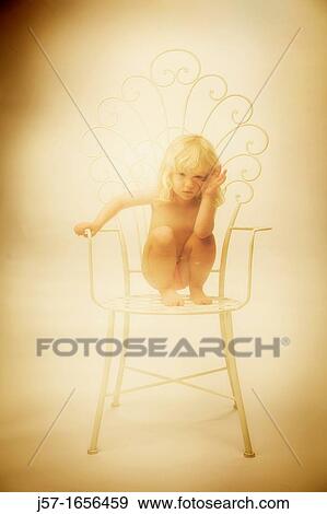 Young girl sitting on a chair in the studio with blond curly hair View Large Photo Image Stock Photo - Young girl sitting on a chair in the studio with blond curly hair. Fotosearch