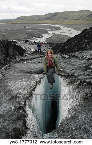 Stock Image - Young girl sitting on glacier by large crevice, Solheimajokull, Iceland. Fotosearch