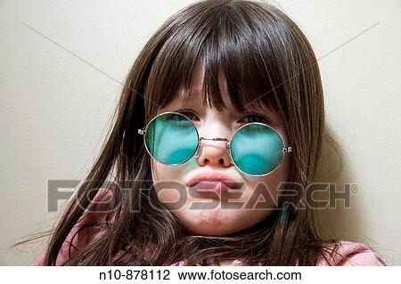 Stock Image - Young girl wearing green colored sunglasses.. Fotosearch