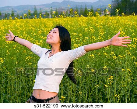 Stock Image - young good looking asian (chinese) girl enjoying the outdoors in a rape field. Fotosearch