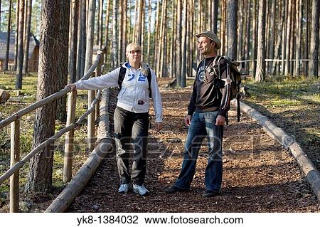 Stock Image - Young Happy Hiking Couple Standing on Wooden Boardwalk Stair in Forest. Fotosearch