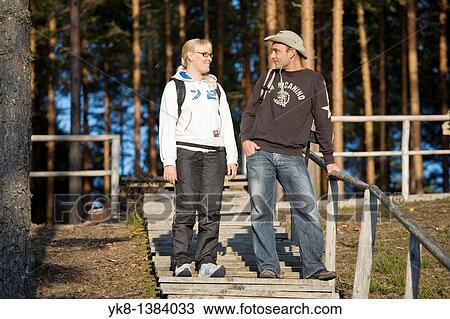 Stock Image - Young Happy Hiking Couple Standing on Wooden Boardwalk Stair in Forest. Fotosearch