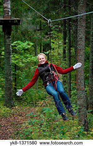 Stock Image - Young happy smiling woman driving on zip wire in adventure park trail in Otep??, Estonia. Fotosearch