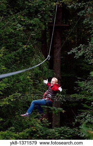 Stock Photo - Young happy smiling woman driving on zip wire in adventure park trail in Otep??, Estonia. Fotosearch