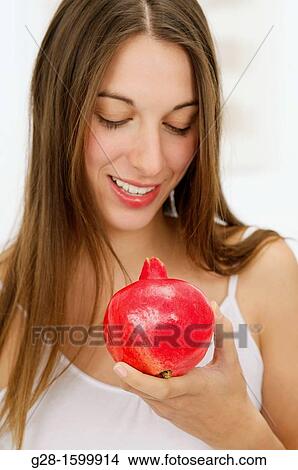 Picture - Young happy woman holding a pomegranate in her hand. Fotosearch