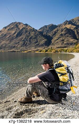 Young hiker sat on the shore at Glendhu Bay gazing out at Lake Wanaka, South Island of New Zealand View Large Photo Image Stock Photo - Young hiker sat on the shore at Glendhu Bay gazing out at Lake Wanaka, South Island of New Zealand. Fotosearch