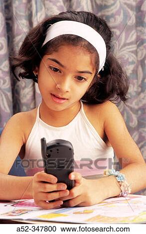 Stock Image - Young Indian girl dialling mobile phone. Fotosearch