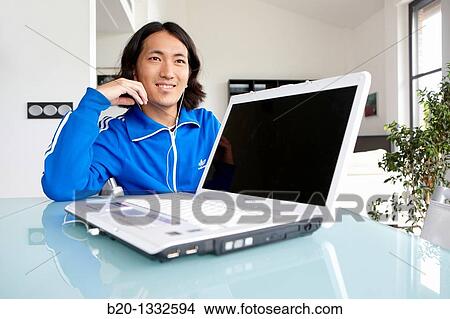 Picture - Young Japanese man with laptop computer in room. Fotosearch