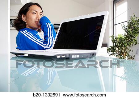 Stock Image - Young Japanese man with laptop computer in room. Fotosearch