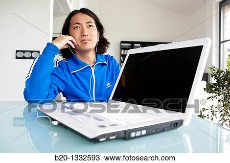 Stock Image - Young Japanese man with laptop computer in room. Fotosearch