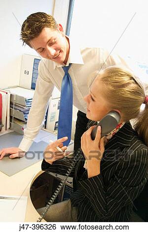 Stock Photograph - Young lady on the phone smiling, with a young man leaning over her shoulder. Fotosearch