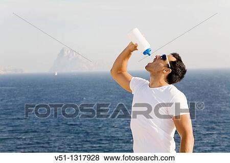Young male runner drinks from a bottle View Large Photo Image Stock Photo - Young male runner drinks from a bottle. Fotosearch