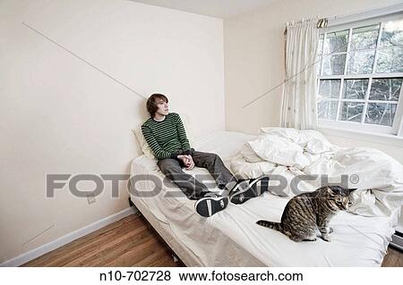 Young man and a cat sitting on his bed. View Large Photo Image Stock Photo - Young man and a cat sitting on his bed.. Fotosearch