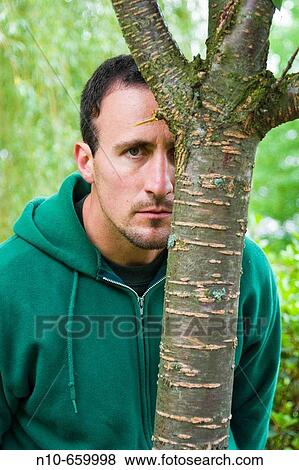 Young man, at a park, looking out from behind a tree. View Large Photo Image Stock Photo - Young man, at a park, looking out from behind a tree.. Fotosearch