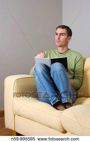 Stock Photography - Young man at home, writing in a journal note book.. Fotosearch