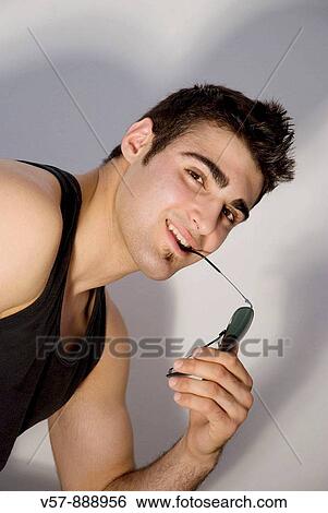 Young man biting his sunglasses, smiling and looking at the camera View Large Photo Image Stock Photograph - Young man biting his sunglasses, smiling and looking at the camera. Fotosearch