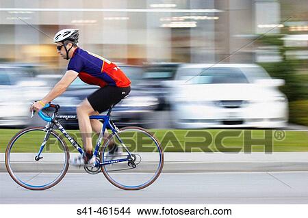Young man cycling, blurred urban background. View Large Photo Image Picture - Young man cycling, blurred urban background.. Fotosearch