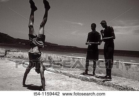 Stock Image - Young man doing handstand on the seawall of Baracoa / Cuba. Fotosearch
