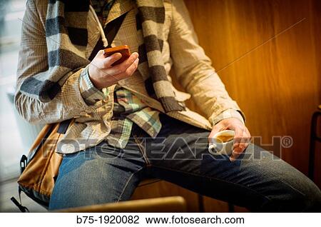 young man dressed casual and relaxed drinking a coffee with a mobile phone in hand View Large Photo Image Stock Image - young man dressed casual and relaxed drinking a coffee with a mobile phone in hand. Fotosearch