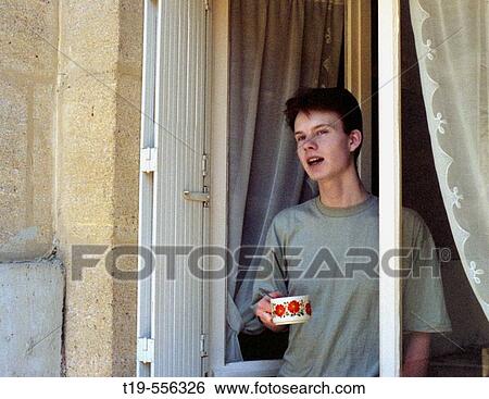 Young man having his morning coffee while looking out the kitchen window View Large Photo Image Stock Photograph - Young man having his morning coffee while looking out the kitchen window. Fotosearch