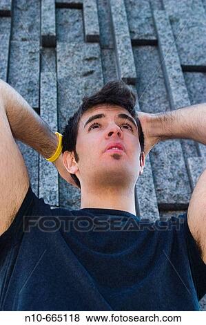 Stock Photo - Young man, his hands on his head, in front of a concrete wall.. Fotosearch
