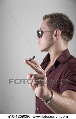 Stock Photograph - Young man holding a thin cigar. Fotosearch