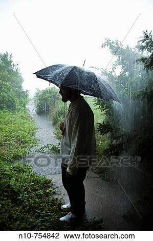 Young man, holding an umbrella, standing in a rainstorm. View Large Photo Image Stock Image - Young man, holding an umbrella, standing in a rainstorm.. Fotosearch