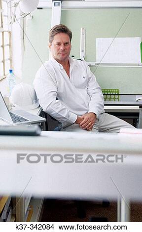Picture - Young man in design studio sitting at draughting table. Proud small business owner. Fotosearch