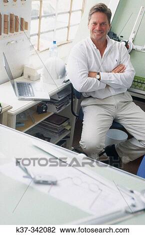 Young man in design studio sitting at draughting table. Proud small business owner View Large Photo Image Stock Image - Young man in design studio sitting at draughting table. Proud small business owner. Fotosearch