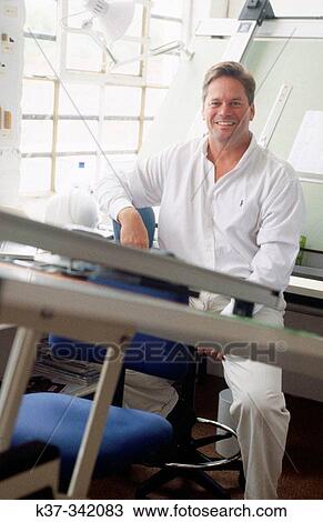 Young man in design studio sitting at draughting table. Proud small business owner View Large Photo Image Stock Image - Young man in design studio sitting at draughting table. Proud small business owner. Fotosearch