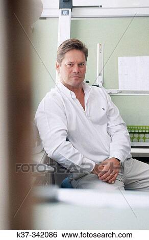 Stock Photograph - Young man in design studio sitting at draughting table. Proud small business owner. Fotosearch