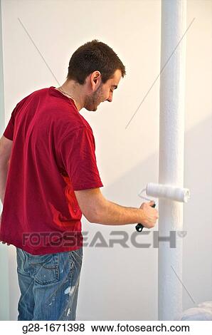 Young man in red T-shirt and stained jeans using a paint roll to paint in white a pillar View Large Photo Image Stock Photo - Young man in red T-shirt and stained jeans using a paint roll to paint in white a pillar. Fotosearch