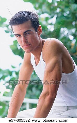 Young man, in white tank top t-shirt, sitting-looking direct with kind confidence View Large Photo Image Stock Image - Young man, in white tank top t-shirt, sitting-looking direct with kind confidence. Fotosearch