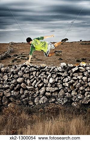 Young man jumping over dry stone wall. Minorca, Balearic Islansd, Spain. View Large Photo Image Picture - Young man jumping over dry stone wall. Minorca, Balearic Islansd, Spain.. Fotosearch