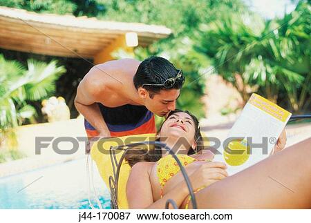 Young man kissing woman on forehead while laying down on chair by the pool View Large Photo Image Stock Photo - Young man kissing woman on forehead while laying down on chair by the pool. Fotosearch