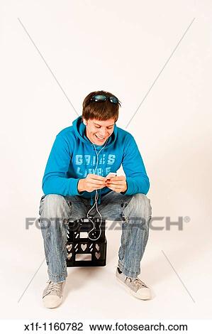 Young man listening to music on his iPod sitting on a plastic crate, UK View Large Photo Image Stock Image - Young man listening to music on his iPod sitting on a plastic crate, UK. Fotosearch