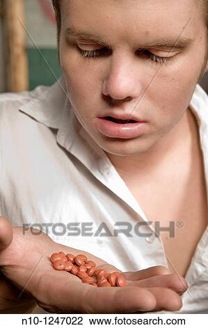 Young man looking at pills in his hand View Large Photo Image Stock Image - Young man looking at pills in his hand. Fotosearch