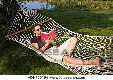 Young man lying in a hammock reading a book in the garden View Large Photo Image Picture - Young man lying in a hammock reading a book in the garden. Fotosearch