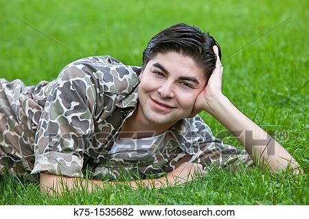 Stock Image - Young man lying in grass smiling for portrait. Fotosearch