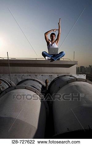 Young man meditating on rooftop, buildings in background View Large Photo Image Stock Image - Young man meditating on rooftop, buildings in background. Fotosearch