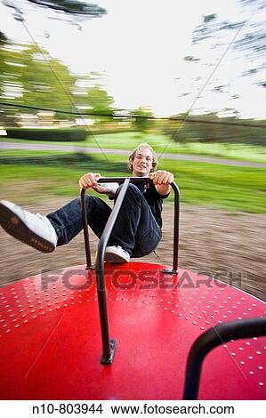 Picture - Young man on a spinning playground ride.. Fotosearch