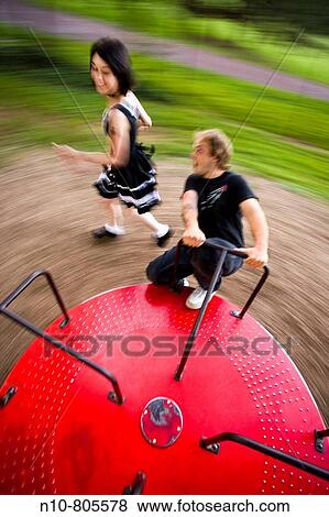 Young man on a spinning playground ride, as his girlfriend runs alongside. View Large Photo Image Stock Photo - Young man on a spinning playground ride, as his girlfriend runs alongside.. Fotosearch