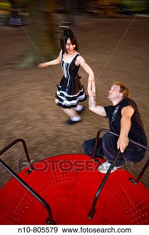 Young man on a spinning playground ride, as his girlfriend runs alongside. View Large Photo Image Stock Photo - Young man on a spinning playground ride, as his girlfriend runs alongside.. Fotosearch