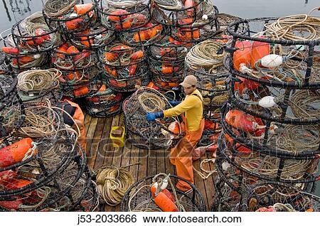 Stock Photograph - Young man on deck of commercial fishing boat preparing crab pots for next trip, Westport, Washington USA.. Fotosearch